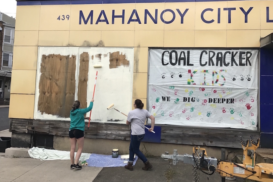 Photo of volunteers using paint rollers to help clean up the facade of the Mahanoy City Lumber Company.