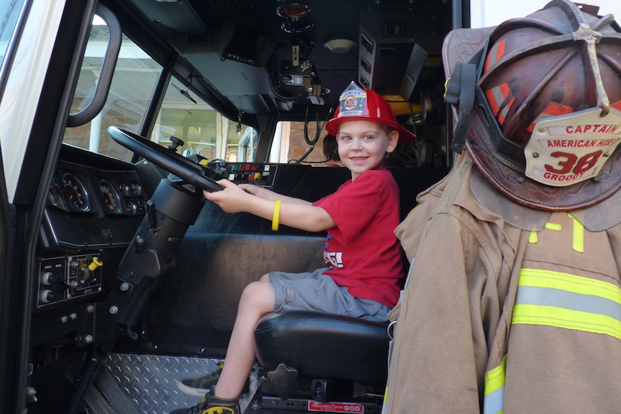 Photo of a young boy behind the wheel of a fire engine.